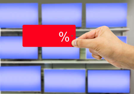 Man holding discount red label with percent sign in hand  with percentage tv shop background and copy spaceの写真素材