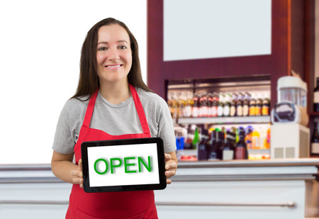 portrait of a barista woman in a coffee shop holding up an signal with open word
