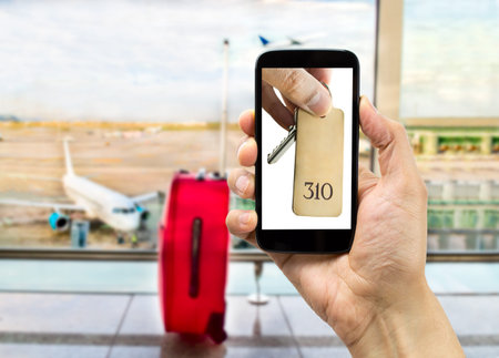 hand holding a smartphone with a picture of hand holding the key of hotel at the airport lounge