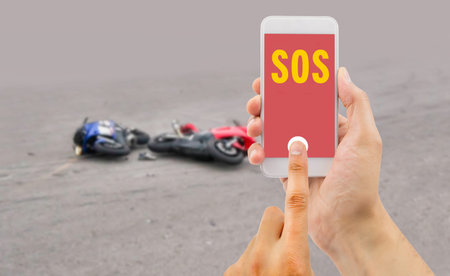 hand holding a cellphone with emergency number SOS on the screen with a motorcycle accident in backgroundの写真素材