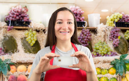 smiling shopwoman showing credit cart with copy space at the fruit shopの写真素材