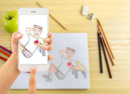 hand of a child holding and using a modern smartphone and making a photo to a picture to send to their parents for mother day and fatherの写真素材