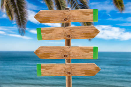 wooden signpost in the meadow with copyspace on the ocean and palms backgroundの写真素材