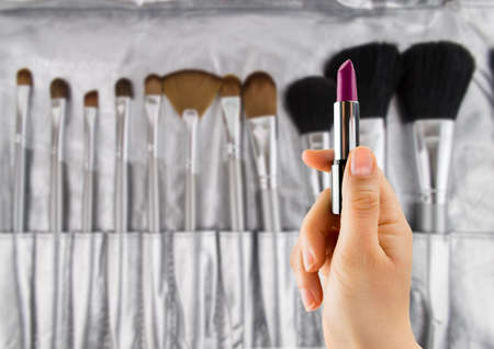 woman holding  fuchsia lipstick with of a set of makeup brushes in the backgroundの写真素材