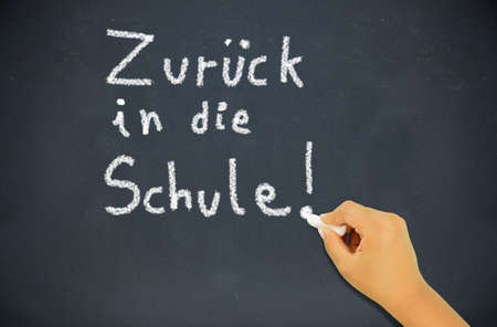 boy writing on a blackboard with chalk phrase Back to school in German - Zur?ck in die schuleの写真素材