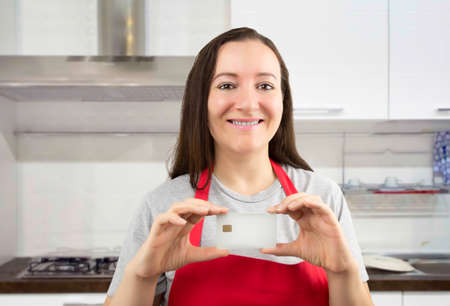 cooker woman showing credit cart in blank with copyspace at the kitchen as concept of domestic economyの写真素材