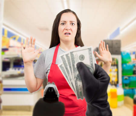 portrait of saleswoman with arms up at the supermarket in a robbery with gunの写真素材