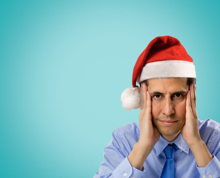 portrait of stressed man wearing red santa hat looking angry and distressed with copyspace on blue backgroundの写真素材