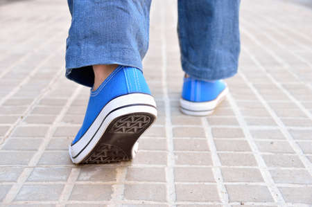 Cropped rear view of a young with sneakers walking along a streetの写真素材