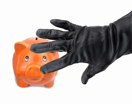 black gloved hand of a thief stealing a piggy bank pig shaped orange and white backgroundの写真素材