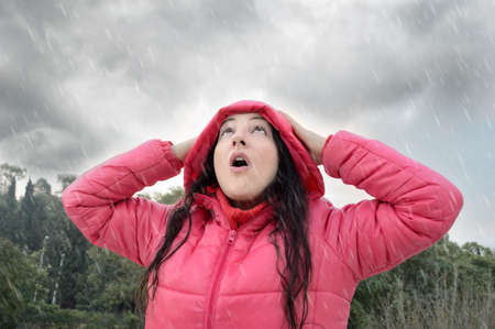 woman with pink coat very happy and looking with surprise to the sky by the rain at the forestの写真素材