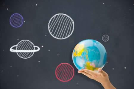 child holding the planet Earth in hand wwith drawing of planets at the bottom of a blackboardの写真素材