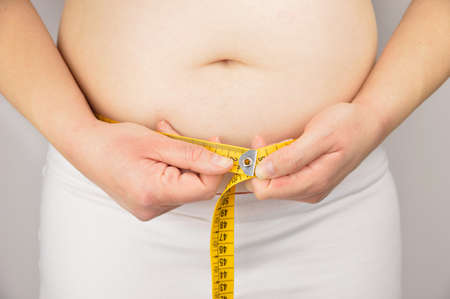 Cropped midsection of an obese woman measuring his waist with a measuring tape against a grey backgroundの写真素材