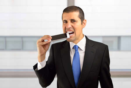 Portrait of a frustrated young businessman biting the cell phone against at officeの写真素材