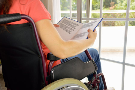 Rear view low section of a patient on a wheelchair at a home reading a bookの写真素材