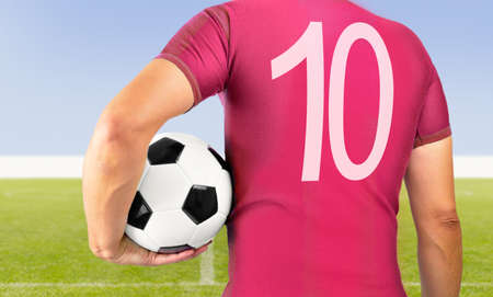 Cropped rearview image of a young player man holding a soccer ball under his arms wearing red shirtの写真素材