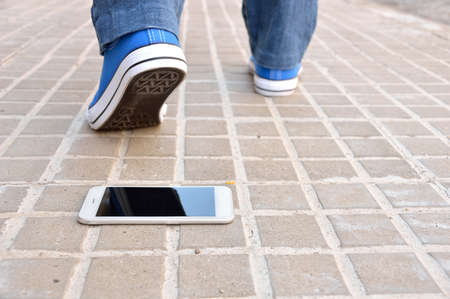Cropped rear view of a walking young who loses the phone falling on the sidewalk street in the cityの写真素材