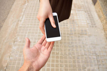woman with a phone in his hand  return it to its owner at the city street. Concept of loan from a phone to help someone.の写真素材