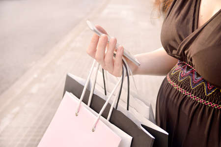 Pregnant woman shopping with a smart phone and carrying shopping bags at the  city street. Concept of a shopaholicの写真素材