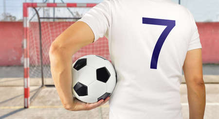 Cropped rearview image of a young player man holding a soccer ball under his arms at empty football court in backgroundの写真素材
