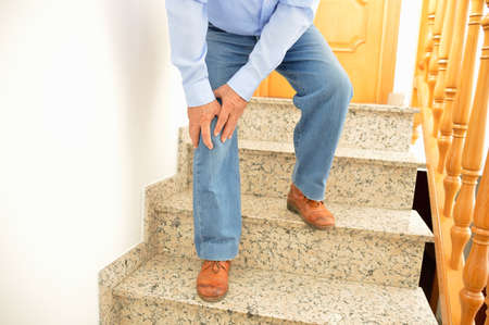 elderly man walking down the stairs at home and touching his knee by the painの写真素材