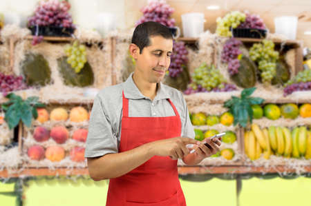shopman with apron uses a smart phone at the fruits storeの写真素材