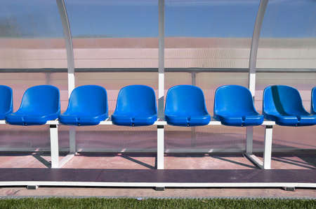 sport bench with red plastic seats in the stadium players outdoors with blue paint under transparent plastic roof as banking playersの写真素材