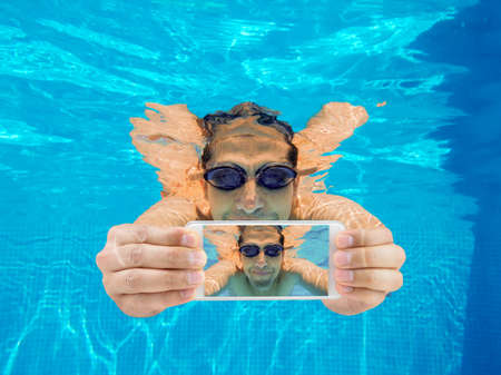 Portrait of a happy man with smart phone under water. Selfiesの写真素材