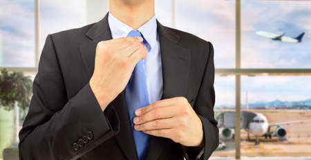 cropped shot of a businessman in a his tie adjusting at airport departure lounge.Business travel conceptの写真素材