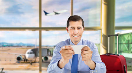 portrait of a businessman playing a video game and connected to social networks by smartphone at the office at airport departure loungeの写真素材
