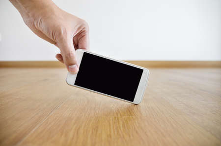 cropped shot of a man locating and catching a phone on the floor at homeの写真素材