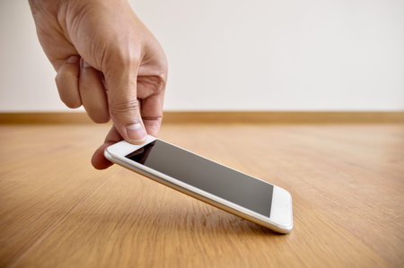 cropped shot of a man locating and catching a phone on the floor at home