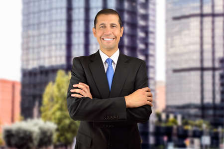 portrait of a businessman standing with his arms folded with office buildings in backgroundの写真素材