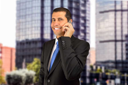 businessman conversating by cellphone with customer and the office buildings in backgroundの写真素材