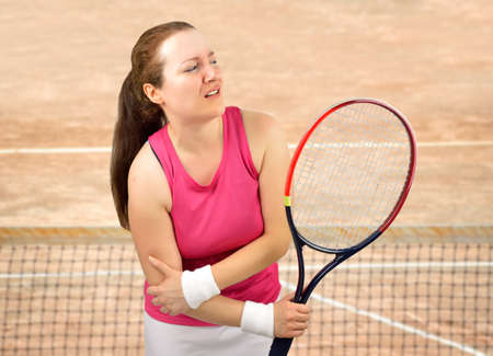 tennis woman player with elbow injury holding the racket on a clay courtの写真素材