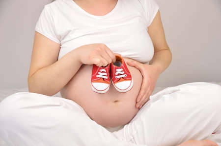 Cropped shot of a woman holding baby shoes against her pregnant belly の写真素材
