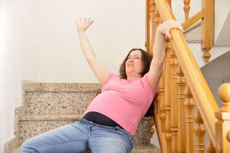 Pregnant woman falling down on stairs with hands up to try to catching the railingの写真素材