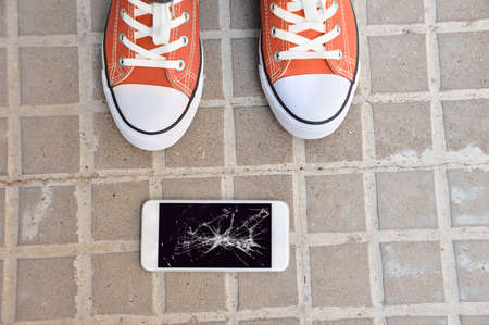 Person picking broken smart phone with cracked screen of the groundの写真素材