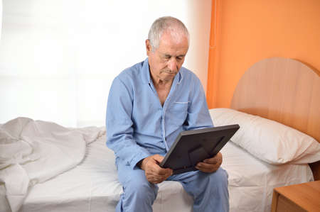 Sad senior man missing her wife after divorce with a picture of the couple の写真素材