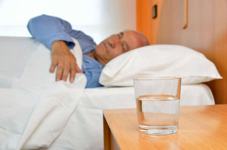 Senior man lying on bed with glass of mineral water on the nightstandの写真素材