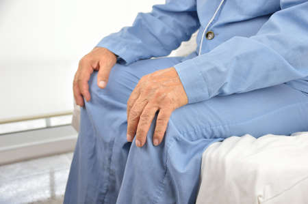 Senior man sitting on bed with his hands on kneesの写真素材