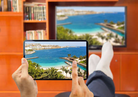 relaxed man with smart tv and tablet connected to a tv and envisioning photos in networking (tv and telephone image from a photo of a beach at Gran canaria from my portfolio)の写真素材