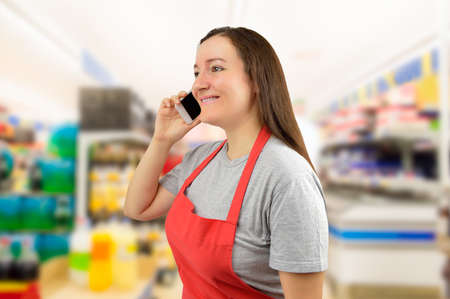 shopwoman with pinafore uses a smart phone at the supermarketの写真素材