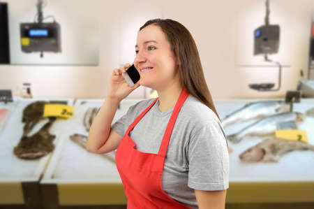 shopwoman with apron using a smart phone at the fishmongerの写真素材