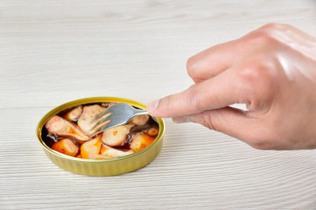 Cropped shot of a man eating a canned of octopus in sauce on rustic wooden table