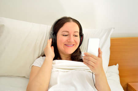 Happy young woman enjoying peaceful music at bedroom resting on theの写真素材