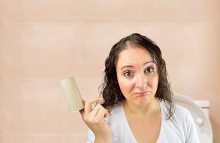 portrait of sad woman that finished toilet paper roll at bathroomの写真素材