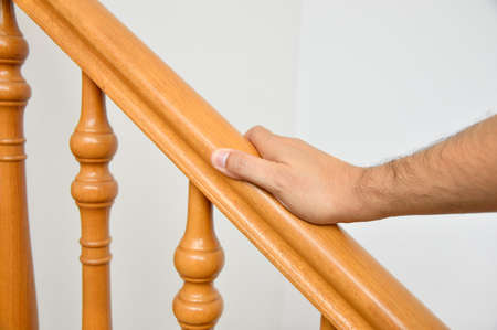 closeup of man using the wooden railing of stairs to go downstairs at his homeの写真素材