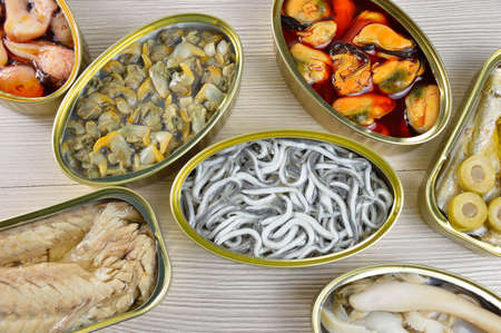 Assortment of cans of canned with different types of fish and seafood on rustic wooden tableの写真素材