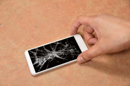 Person picking broken smart phone with cracked screen on the floor at homeの写真素材